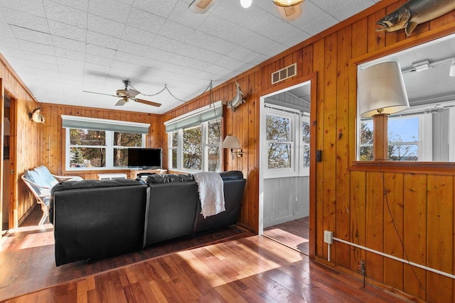 living room with dark wood-type flooring, ceiling fan, and wood walls