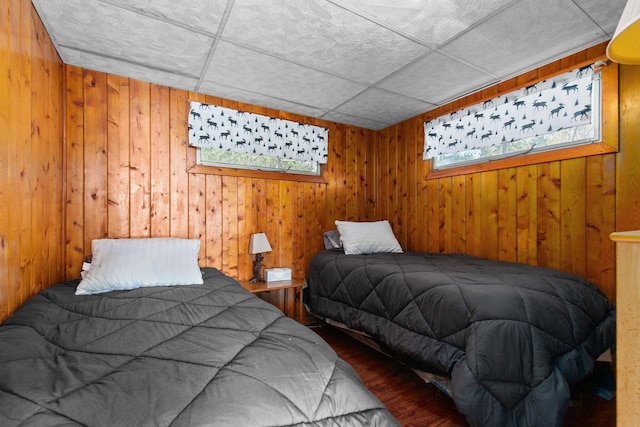 bedroom featuring wooden walls, a drop ceiling, and wood-type flooring