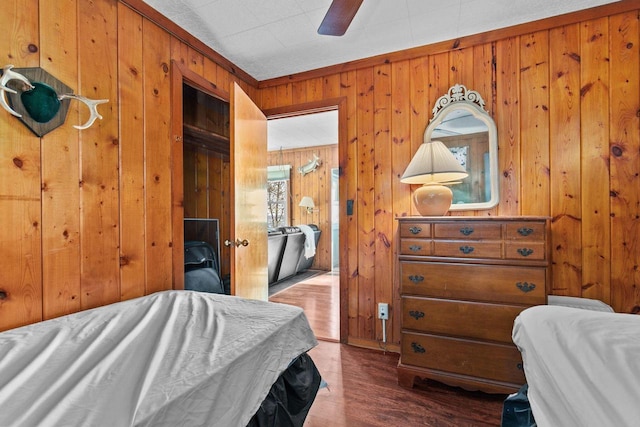 bedroom featuring crown molding, wooden walls, dark wood-type flooring, and ceiling fan