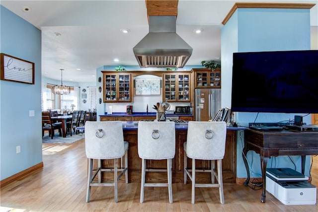 kitchen with light hardwood / wood-style flooring, island exhaust hood, stainless steel fridge, decorative light fixtures, and a breakfast bar