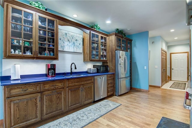 kitchen with appliances with stainless steel finishes, light hardwood / wood-style flooring, sink, and backsplash