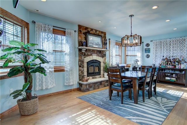 dining area with a stone fireplace, an inviting chandelier, and hardwood / wood-style floors