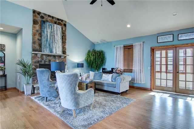 living room featuring lofted ceiling, ceiling fan, light wood-type flooring, a fireplace, and french doors