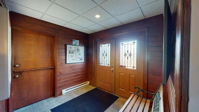 carpeted entryway with a drop ceiling, baseboard heating, and wooden walls