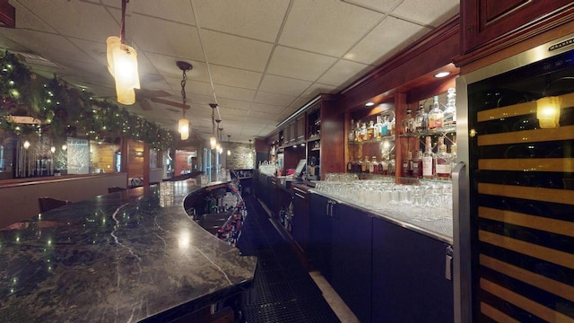 bar featuring wine cooler, a paneled ceiling, pendant lighting, and dark stone countertops