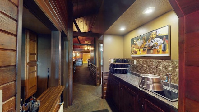 bar with decorative backsplash, sink, dark carpet, and a textured ceiling