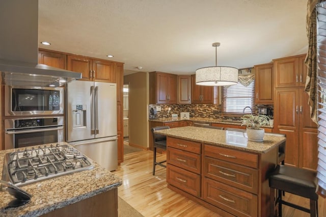 kitchen with a breakfast bar, a center island, pendant lighting, appliances with stainless steel finishes, and light hardwood / wood-style floors