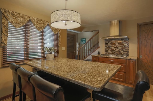 kitchen featuring wall chimney range hood, stainless steel gas stovetop, decorative light fixtures, and a breakfast bar area