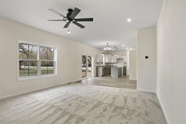 unfurnished living room featuring light carpet, sink, and ceiling fan with notable chandelier