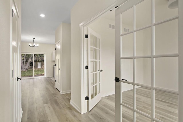 corridor with light hardwood / wood-style floors and an inviting chandelier