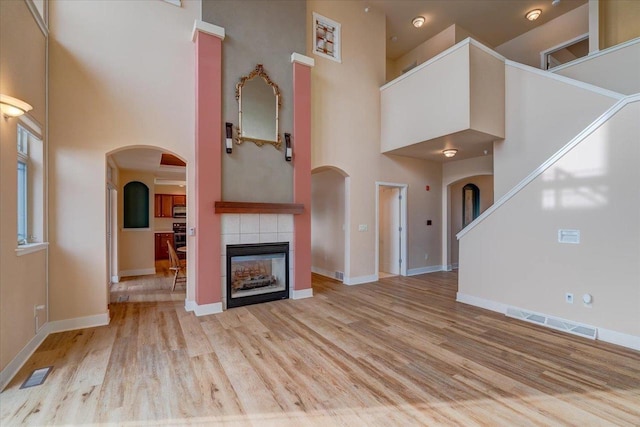 unfurnished living room featuring a fireplace, light hardwood / wood-style floors, and a high ceiling