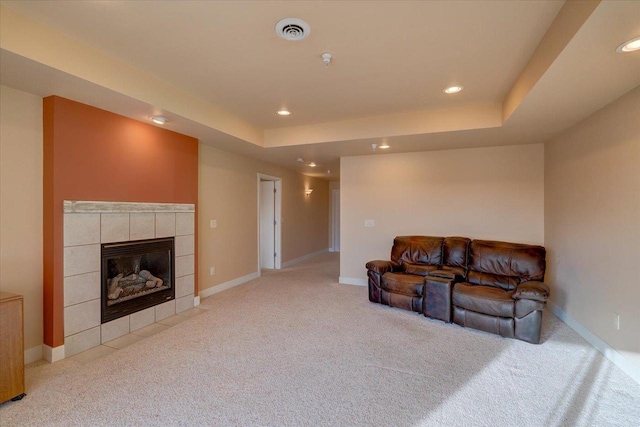 living room featuring a raised ceiling, light carpet, and a fireplace