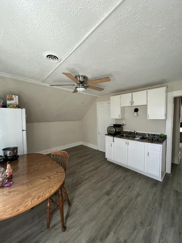 kitchen with dark wood-type flooring, vaulted ceiling, white cabinetry, white fridge, and ceiling fan