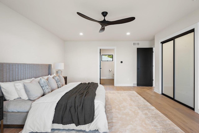 bedroom featuring light wood-type flooring, a closet, ensuite bath, and ceiling fan