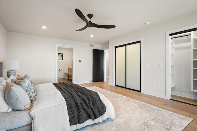 bedroom with light hardwood / wood-style floors, ensuite bath, ceiling fan, and multiple closets