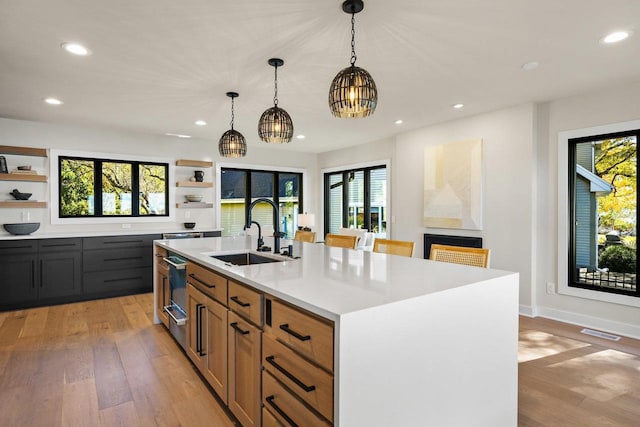 kitchen with sink, an island with sink, a chandelier, decorative light fixtures, and light wood-type flooring