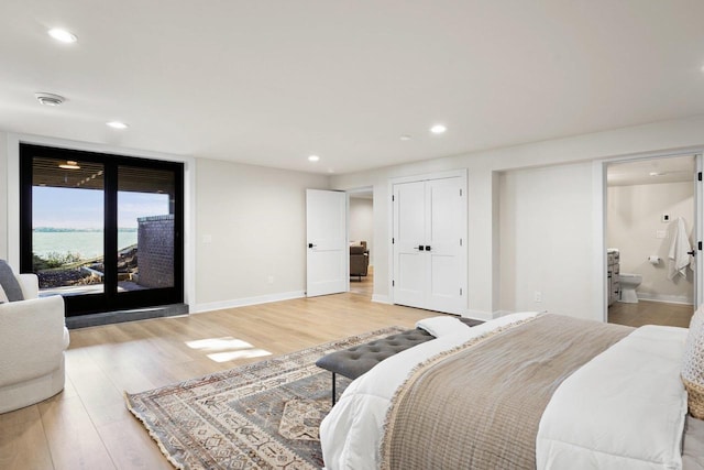 bedroom featuring light hardwood / wood-style floors, a water view, access to outside, and ensuite bath