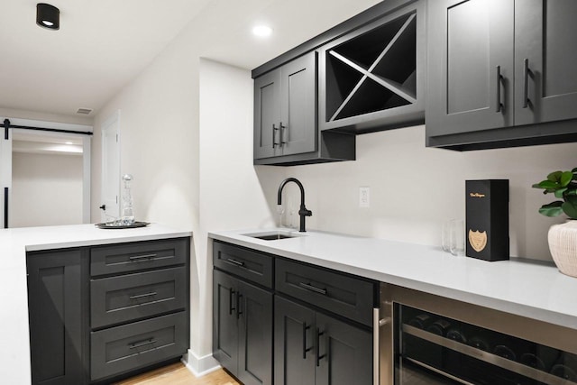 kitchen with a barn door, sink, beverage cooler, and light hardwood / wood-style floors