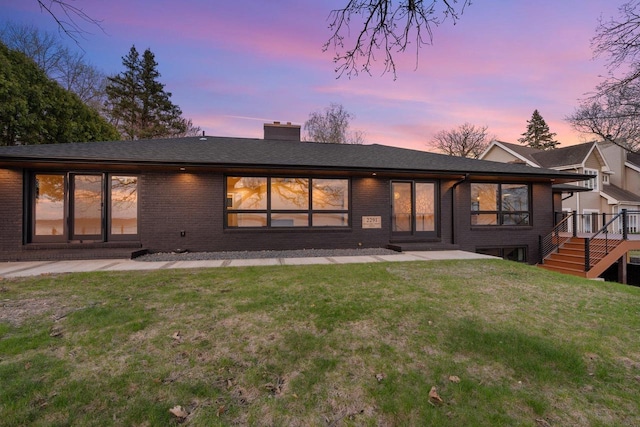2291 Williams Point Dr, Stoughton, WI 53589 - back of house at dusk featuring brick siding, a chimney, a yard, and stairway