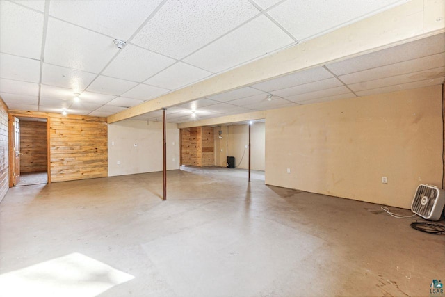 basement featuring a paneled ceiling and wood walls