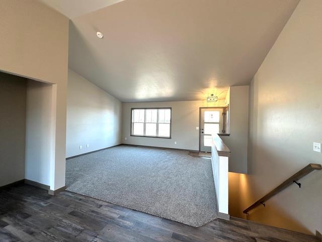 unfurnished living room with dark wood-style floors, baseboards, and vaulted ceiling