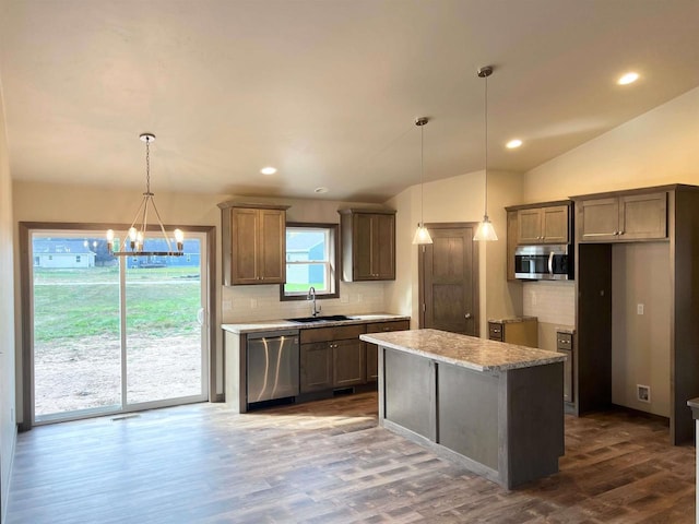 kitchen with dark wood finished floors, lofted ceiling, a sink, appliances with stainless steel finishes, and a center island