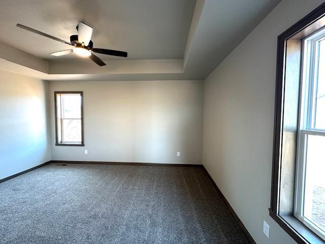 carpeted empty room with a ceiling fan, a raised ceiling, and baseboards