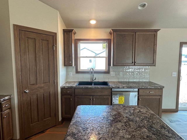 kitchen featuring baseboards, dark stone counters, a sink, stainless steel dishwasher, and backsplash