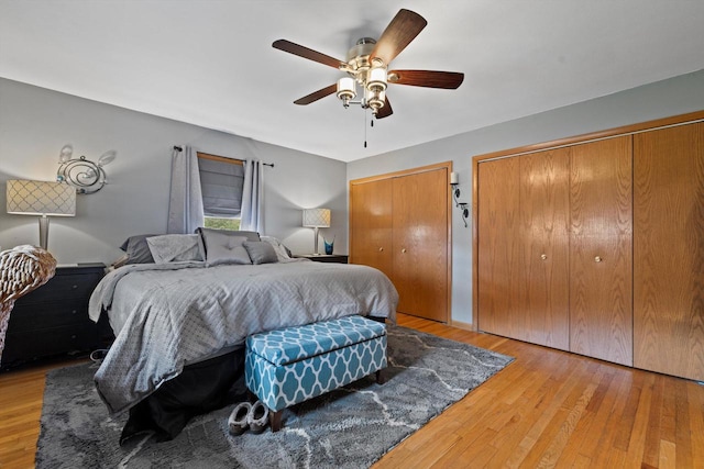 bedroom with two closets, hardwood / wood-style flooring, and ceiling fan