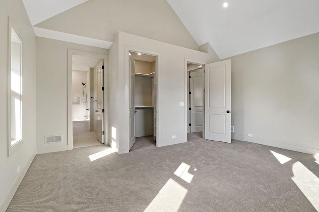 unfurnished bedroom featuring lofted ceiling, a walk in closet, a closet, ensuite bath, and light colored carpet