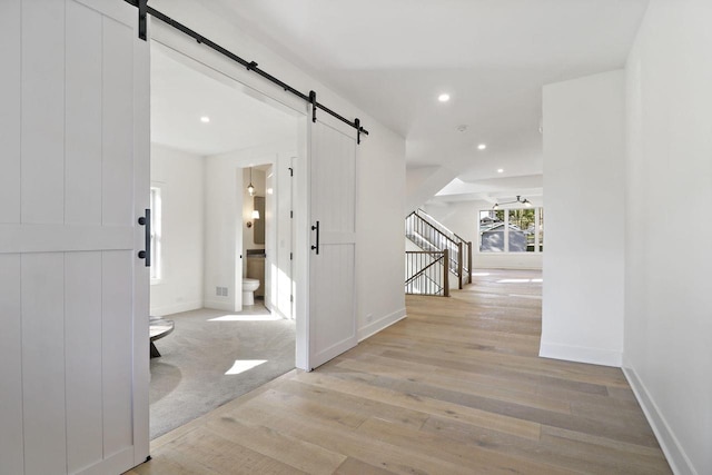 corridor featuring light wood-type flooring and a barn door