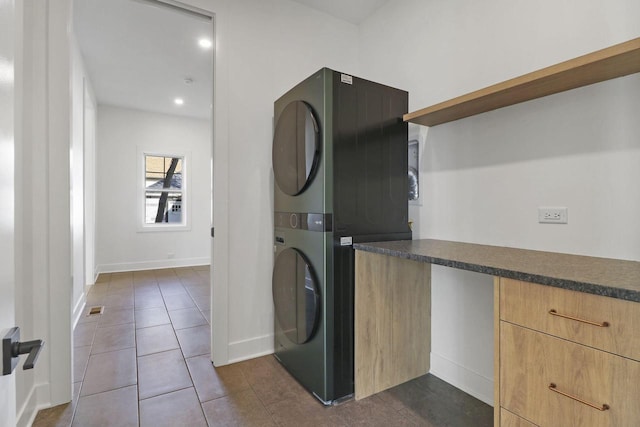 laundry room with dark tile patterned floors, stacked washer and dryer, and cabinets