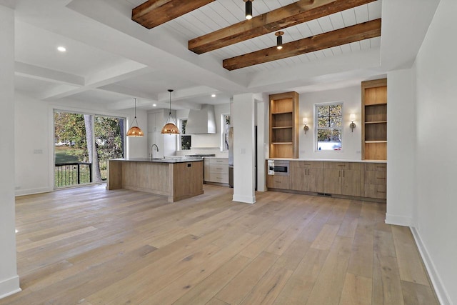 kitchen with wall chimney range hood, beamed ceiling, hanging light fixtures, a large island, and light wood-type flooring