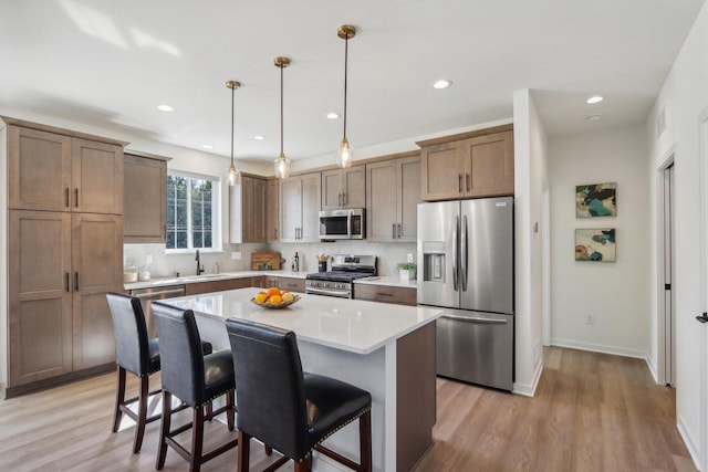 kitchen featuring hanging light fixtures, appliances with stainless steel finishes, a kitchen breakfast bar, light wood-type flooring, and a center island