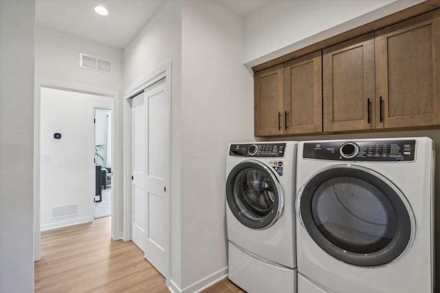 laundry area featuring light hardwood / wood-style flooring, washing machine and dryer, and cabinets