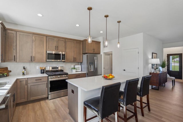 kitchen featuring a breakfast bar area, appliances with stainless steel finishes, light wood-type flooring, decorative light fixtures, and a center island