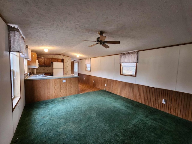 interior space featuring carpet flooring, a textured ceiling, kitchen peninsula, vaulted ceiling, and white refrigerator