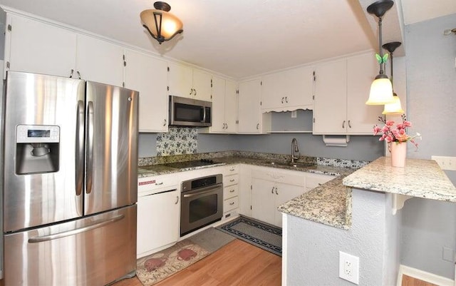 kitchen featuring hanging light fixtures, sink, white cabinets, appliances with stainless steel finishes, and light hardwood / wood-style floors