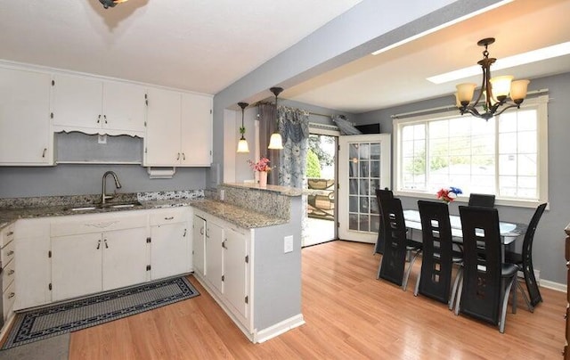 kitchen with sink, light hardwood / wood-style floors, white cabinetry, and decorative light fixtures