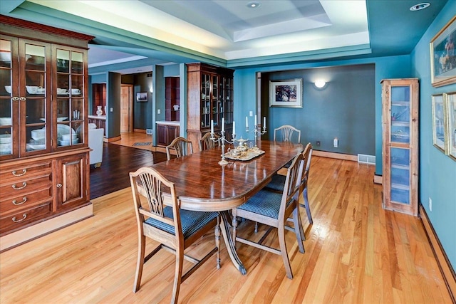 dining area with a raised ceiling and light wood-type flooring