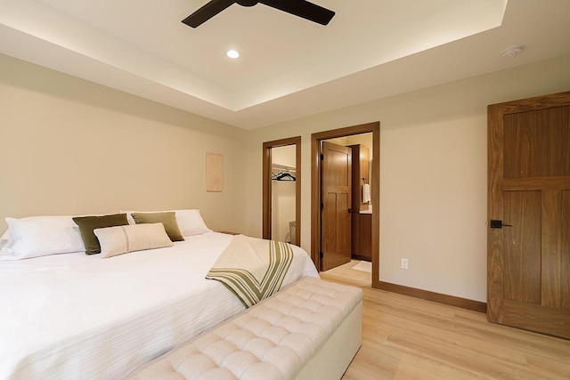 bedroom featuring light hardwood / wood-style floors, ensuite bathroom, a tray ceiling, and ceiling fan