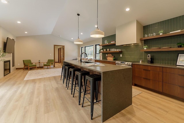 kitchen featuring lofted ceiling, a kitchen island with sink, light hardwood / wood-style flooring, custom exhaust hood, and tasteful backsplash