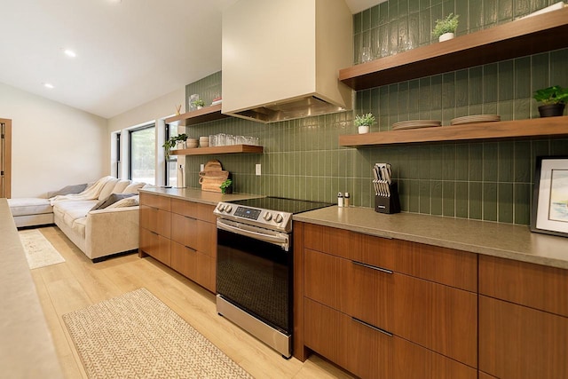 kitchen with light wood-type flooring, lofted ceiling, custom exhaust hood, stainless steel electric range oven, and decorative backsplash