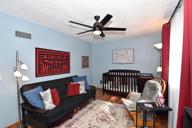 bedroom with a nursery area, hardwood / wood-style flooring, and ceiling fan