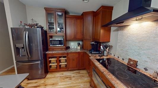 kitchen with light stone countertops, wall chimney exhaust hood, tasteful backsplash, light hardwood / wood-style flooring, and appliances with stainless steel finishes