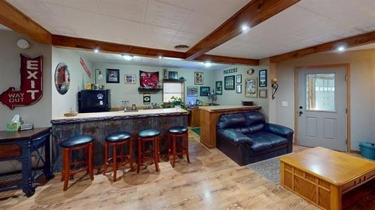 bar with beamed ceiling, black fridge, and light hardwood / wood-style flooring