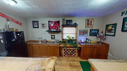 bar featuring black refrigerator and light hardwood / wood-style flooring