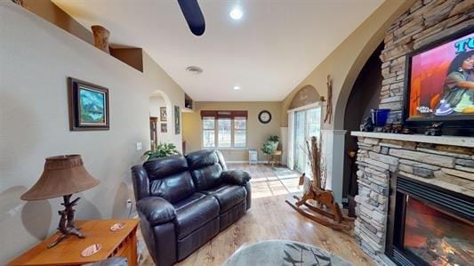 living room featuring ceiling fan, a stone fireplace, and light hardwood / wood-style flooring