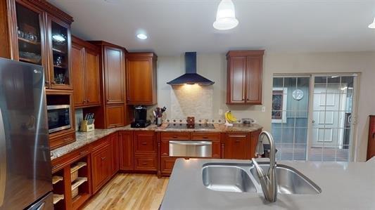 kitchen with appliances with stainless steel finishes, sink, wall chimney range hood, light hardwood / wood-style flooring, and hanging light fixtures