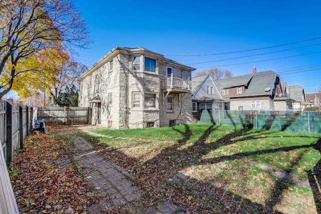 rear view of property featuring a balcony and a yard